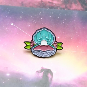 Close-up of enamel pin with shell, pearl and pink floral details on dreamlike background