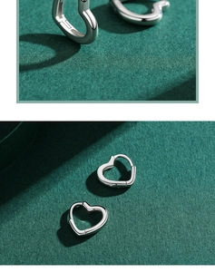Détail de créoles en argent en forme de cœur sur un fond de tissu vert foncé texturé