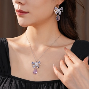 Detailed close-up of zircon bow pendant and matching waterdrop earrings on female model