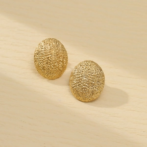 Close-up of matte gold oval earrings with granular texture on light wood background