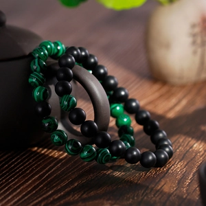 Matte black onyx and green malachite beaded bracelets on a dark ceramic teapot
