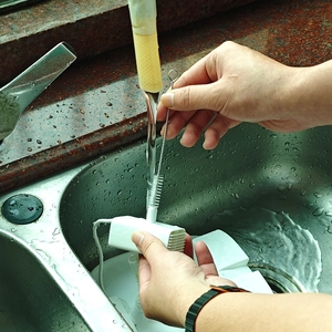Close-up of hands cleaning a white plastic water pump with a thin brush in a sink