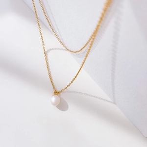 Detailed view of single white pearl pendant on a delicate gold layered chain necklace