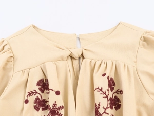 Detail of neckline with delicate red floral embroidery and tie-knot on beige dress
