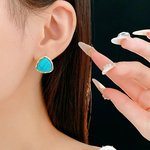 Detail of vintage turquoise triangle earring with gold textured frame worn by a model