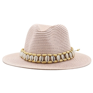 Detail of light pink straw hat with shell and wood bead trim on a woven fedora band