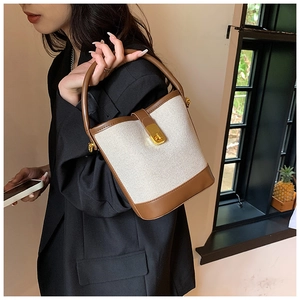 Detail of contrast stitching on brown leather and beige canvas bucket bag with gold lock
