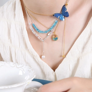Mehrlagige Goldhalskette mit blauem Schmetterlingsanhänger, Perlen und Kristallen an Model
