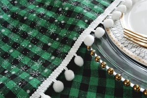 Close-up of green and black plaid tablecloth with white snowflake prints and pompom fringe