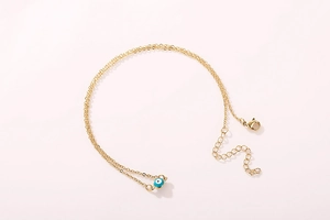 Detail of double-layer gold chain with blue evil eye pendant and lobster clasp closure