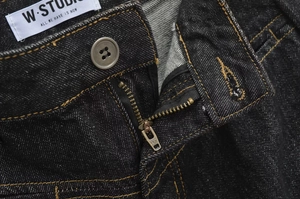 Dettaglio ravvicinato della cerniera YKK e cuciture gialle a contrasto su jeans neri