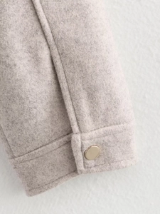 Close-up of oatmeal wool jacket cuff with a polished gold round metal button detail