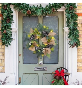 Close-up of Christmas wreath with warm LED lights, pine cones and burlap bow on door