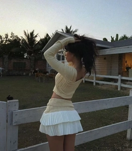 Detail of yellow knit crop top and layered pleated skirt worn in a natural farm setting