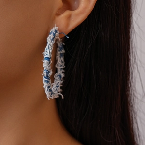 Close-up of model wearing large geometric denim hoop earrings with frayed edge textures