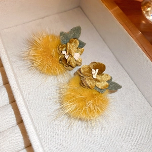 Detail of yellow plush ball earrings with gold and green 3D floral accents in box