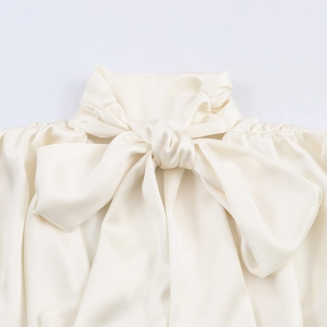 Close-up of elegant bow tie neckline on beige satin blouse with pleated details