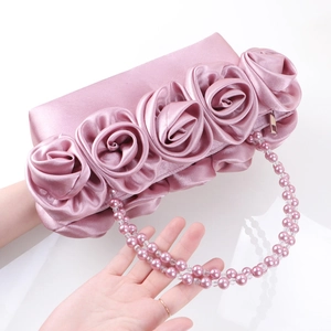 Borsa in raso rosa con rose in tessuto 3D e catena di perle rosa su uno sfondo bianco