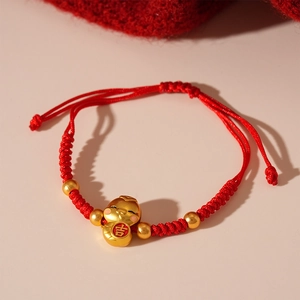 Close-up of red braided rope bracelet featuring a golden 'Ji' lucky pendant and beads