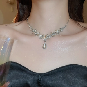 Macro view of crystal teardrop pendant and wheat leaf necklace on a dark satin background