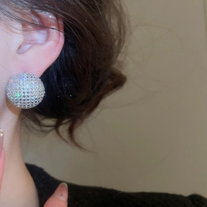 Macro view of sparkly zircon paved spherical stud earrings worn on a female model