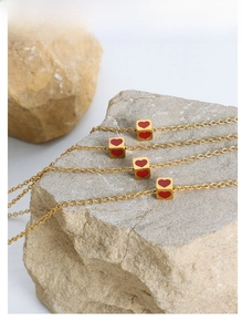 Detail of four gold necklaces with square heart pendants on natural textured stones