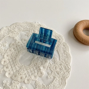 Close-up of a blue glittery acetate hair claw clip resting on a white lace fabric