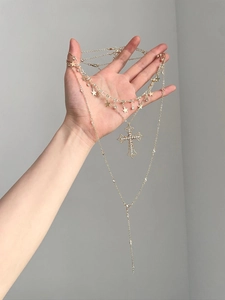 Detail showing multi-layer gold chain necklace with star charms and a rhinestone cross pendant