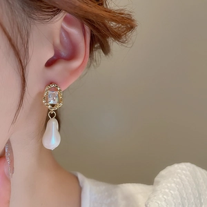 Detail of vintage gold earrings with zircon inlay and baroque pearls on a model
