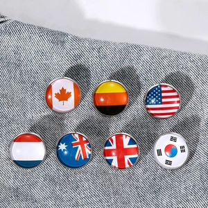 Collection of seven round national flag pins displayed on grey denim fabric texture