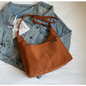 Detail of caramel nylon crossbody bag featuring front pockets and brown fashion leather patch