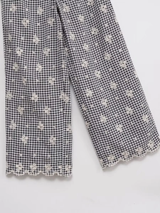 Détail de broderies florales blanches et ourlet festonné sur un pantalon à carreaux