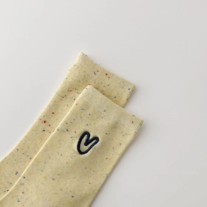 Detail of yellow speckled socks with heart embroidery on a minimalist white background