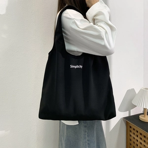 Détail d'un grand sac cabas noir en toile avec lettrage Simplicity porté par un mannequin