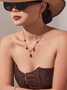 Détail d'un collier doré avec pendentifs coccinelle et piment et boucles d'oreilles torsadées