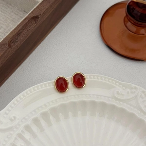Macro view of oval red agate stud earrings with gold plating on a vintage ceramic plate