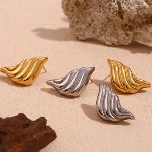 Abstract ripple wing earrings in 18K gold and silver finishes on natural stone background