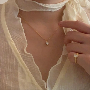 Close-up of a gold heart pendant necklace and square zircon ring on a model