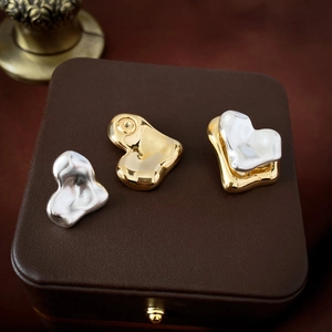 Irregular metal heart earrings in gold and matte silver finishes on leather display