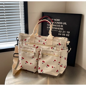 Close-up of canvas tote bag with cherry print, multi-pocket design and long strap