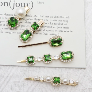 Close-up of five emerald rhinestone hairpins with pearls and crystals in gold setting