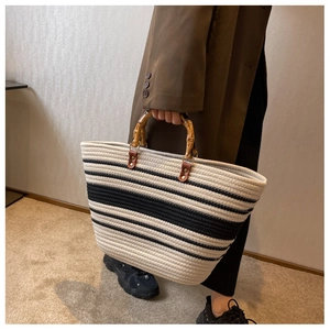 Detail of striped woven tote bag featuring natural bamboo handles and leather accents