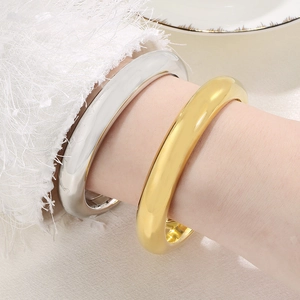 Polished gold and silver 13mm thick stainless steel hollow bangles on a model wrist