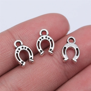 Three tiny silver horseshoe pendants for DIY jewelry shown on a finger for scale
