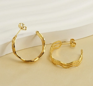 Detail showing the wavy texture and polished gold finish of C-shaped hoop earrings