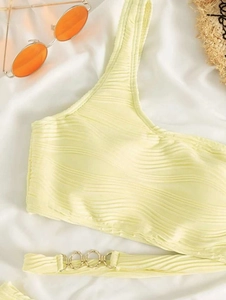 Detail of light yellow one-shoulder bikini with wavy texture and gold ring accent