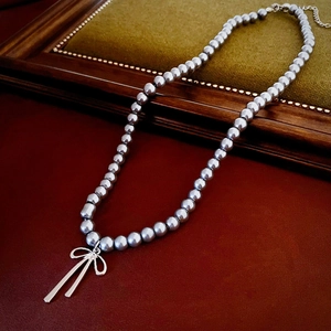 Detailed view of grey faux pearl necklace with silver bow pendant on vintage leather