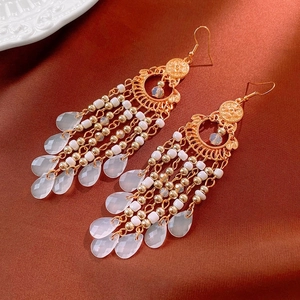 Détail de boucles d'oreilles bohèmes dorées avec perles blanches et glands sur soie