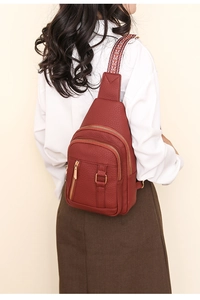 Detail of burgundy PU leather crossbody bag with colorful woven strap on a model