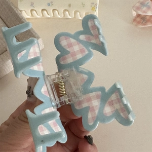 Detail of a blue matte hair claw clip featuring pink and white checkered heart patterns